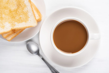 Cup of coffee and sliced bread with honey topping on white table, top view