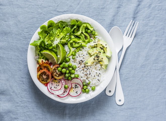 Coconut rice and vegetables buddha bowl. Vegetarian healthy lunch - rice, salad, avocado, radish, tomatoes on a blue background, top view
