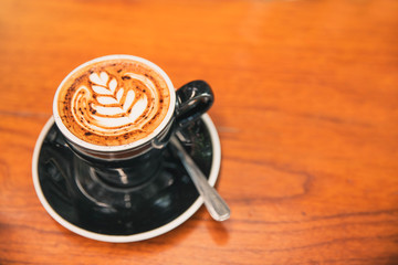 A Cup of hot latte art coffee on wooden table. Hot milk art coffee on wooden background.