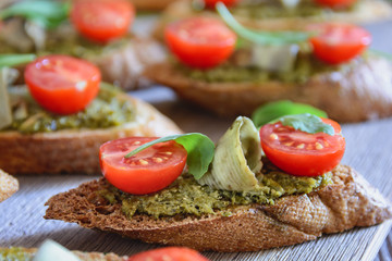 Toasts with pesto sauce, cherry tomatoes, avocado chips and leaves of arugula on a wooden table ready for eating