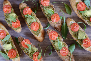 Toasts with pesto sauce, cherry tomatoes, avocado chips and leaves of arugula on a wooden table ready for eating