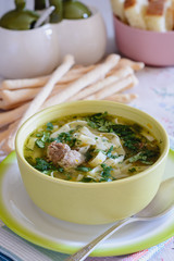 Noodle soup in a deep plate is on the dining table next to bread sticks 