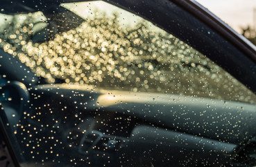 Raindrops on a silver car on the right side and windshield with visible steering wheel and car dashboard.