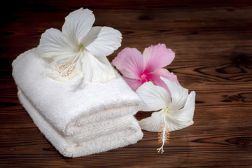 Obraz na płótnie Canvas white cotton towels folded and flowers of hibiscus on wooden background, close up