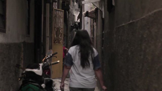 South east asian woman walks while carrying plastic bag in an alley, somewhere in Jakarta