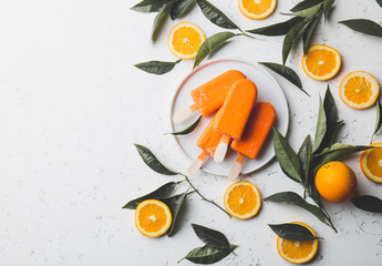 Flat lay of orange popsicle, fresh orange fruits and orange tree leaves, White background