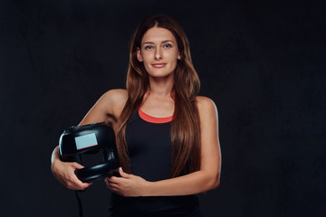 Portrait of a beautiful brunette female boxer in sportswear holds a protective helmet, looking at a camera. Isolated on dark textured background.