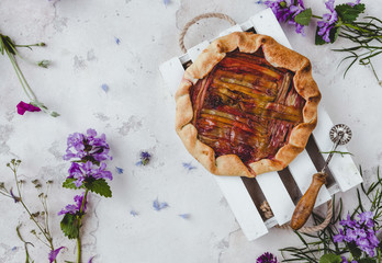 top view of delicious rhubarb pie and scattered flowers on table