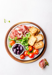Antipasto Plate with dried bread, ham serrano, tomato cherry and purple olives. White background.