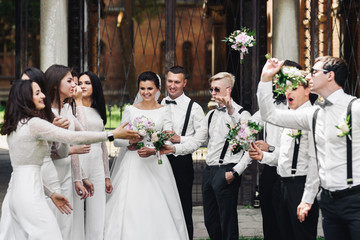 Bridesmaids and groomsmen throw their bouquets over newlyweds posing outside