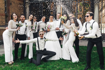 Newlyweds and friends open a bottle of champagne posing on the green lawn