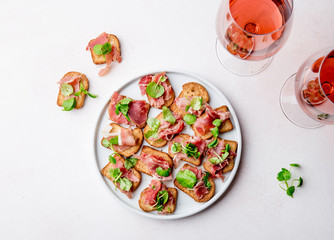 Mini open sandwiches with jamon serrano on white plate and rose wine