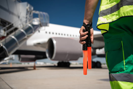 Heading to aircraft. Close up of airport worker arm with marshalling wands. Runway and passenger plane on blurred background