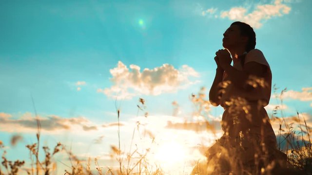 Girl folded her hands in prayer silhouette at sunset. woman praying on her knees. slow motion video. Girl folded her hands in prayer pray to God. the girl praying asks forgiveness for sins of