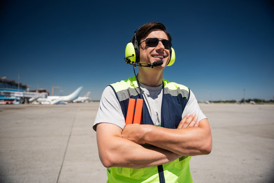 Enjoying beautiful sunny day. Waist up portrait of smiling man in headphones and sunglasses. Blue sky, runway and planes on background