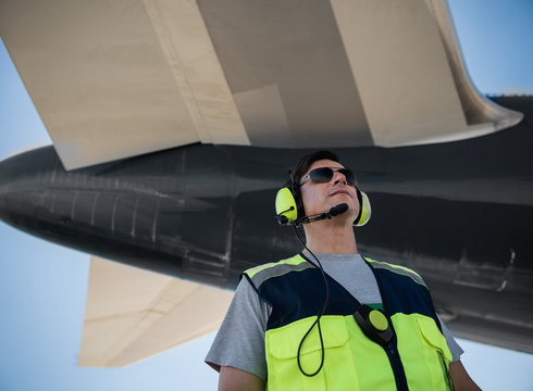Looking up. Low angle portrait of serene man in sunglasses posing at airport. Blue sky and aircraft tail on background
