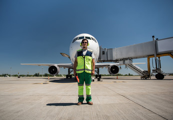 Beautiful day at airdrome. Full length portrait of airport worker standing on runway near passenger plane