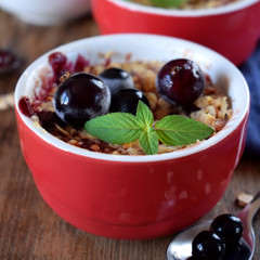Crumble with berries in portion ceramic bowls topped with black currant and mint