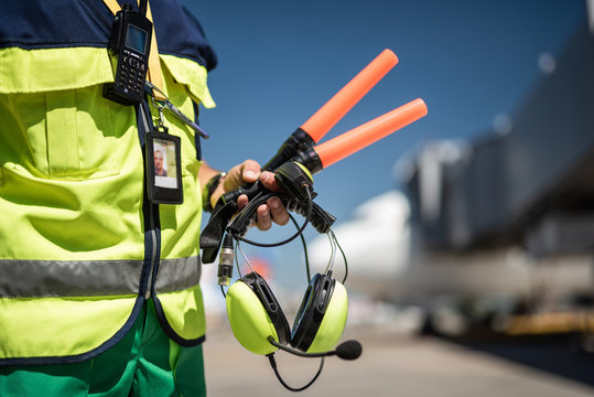 Waiting for plane. Close up of airport worker torso in vest and arm with headset. Airdrome on blurred background
