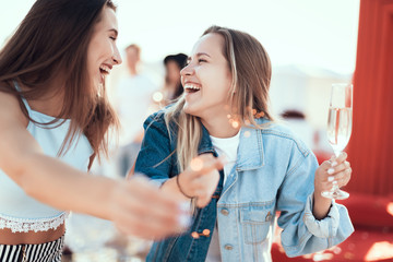 Side view beaming girl telling with outgoing woman while drinking alcohol liquid. They...