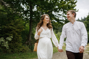 Happy pregnant family having fun time in summer nature. 
