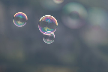 Three soap bubbles flying through the air on a blurry dark gray background