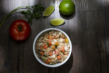 Tabule, comida libanesa tradicional, servida em uma tigela de porcelana branca acompanhada de limão e tomate sobre a mesa de madeira rústica