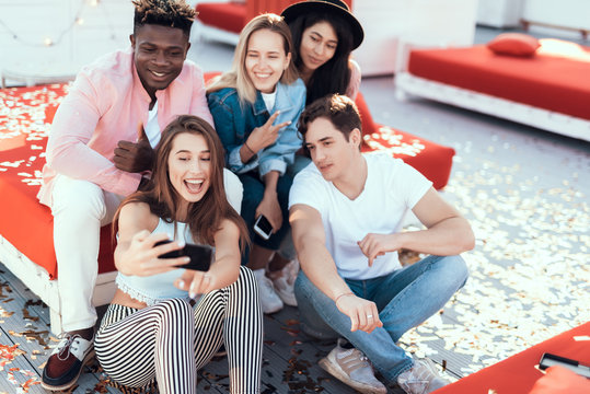 Portrait of satisfied young women and cheerful males taking selfie on mobile. Happy girl holding gadget in hands