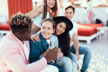 Happy girls talking with outgoing males while resting on comfortable couch outside. They tasting beverage