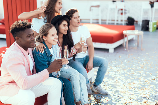 Positive ladies communicating with smiling men. Happy comrades relaxing on cozy sofa while drinking alcohol liquid outdoor