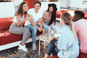 Satisfied girls speaking with cheerful males while sitting on comfortable couch. They tasting alcohol beverage