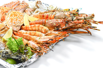 Grilled Mixed Seafoods Big Set contain Lobsters Clams Fish Blue Clabs Big Shrimps Mussels & Calamari Squids with pieces of lemon & vetgetables on white background with shadow Macro Close up side view.