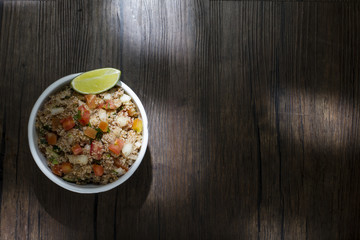 Tabule, comida libanesa tradicional, servida em uma tigela de porcelana branca acompanhada de limão e tomate sobre a mesa de madeira rústica
