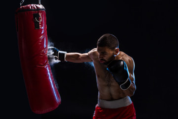 Bearded male boxer training with punching bag on black background. Male boxer as exercise for the...
