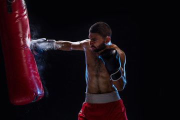 Fototapeta na wymiar Bearded male boxer training with punching bag on black background. Male boxer as exercise for the big fight.