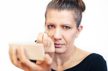 A good middle-aged woman draws her eyelashes. The woman has a sad look, she's sorry for her youth