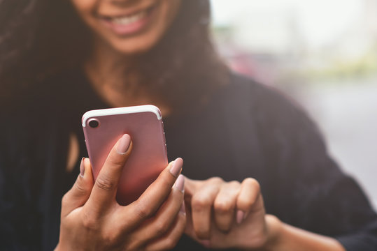 Closeup image of a beautiful mixed race woman holding, using and looking at smart phone.
