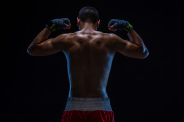 Fototapeta na wymiar Rear view of strong young male boxer. Fitness male model wearing boxing gloves standing on black background.