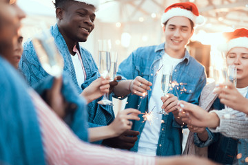 Pleased men and smiling girls keeping bright firework sparklers in hands while drinking appetizing glasses of champagne