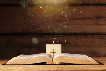 Burning candle and cross on wooden background