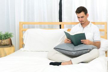 Fototapeta premium Handsome man reading book on the bed in bedroom. Concept of lifestyle, relax and holiday.