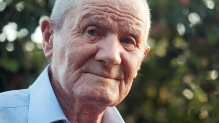 Very old man portrait with emotions. Grandfather is smiling and looking to camera. Portrait: aged, elderly, senior. Close-up of old man sitting alone outdoors. Slow motion. 4k - Powered by Adobe