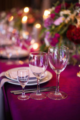 Elegant magenta color wedding banquet table with glasses, dishes and flowers decoration indoors in restaurant. Close up. Wedding decoration concept