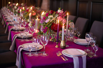 Elegant dark pink wedding banquet table with glasses, dishes and flowers decoration indoors in...