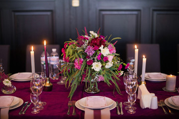 Elegant magenta color velvet table cloth on beautiful wedding table with dishes, candles and flowers. Restaurant. Wedding decoration concept
