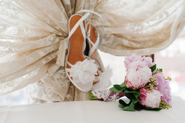 Wedding bouquet and brides high-heel shoes near the lace curtains. Wedding decoration concept.