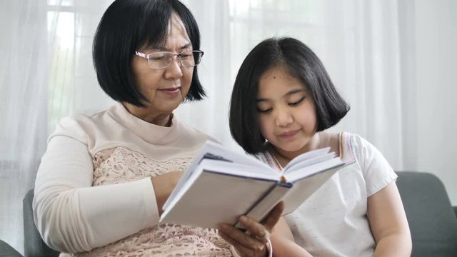 4K Happy Asian grandmother and lovely girl reading book together at home, 60 fps