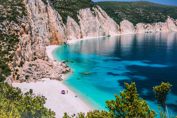 Amazing Fteri beach lagoon, Kefalonia, Greece. Tourists under umbrella chill relax near clear blue...