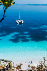 White catamaran yacht at anchor on clear azure surface with dark pattern in calm blue lagoon....