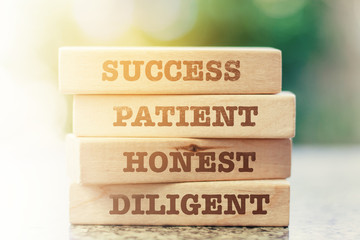 Stack of the wooden toy with word: SUCCESS, PATIENT, HONEST and DILIGENT against blurred natural green background for business and management concept